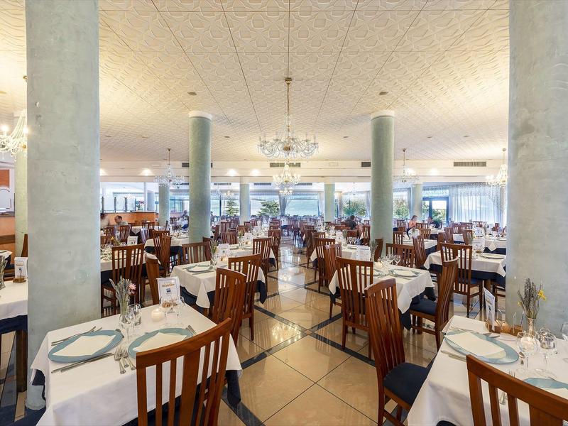 Velká světlá jídelna s elegantně prostřenými stoly a dřevěnými židlemi.