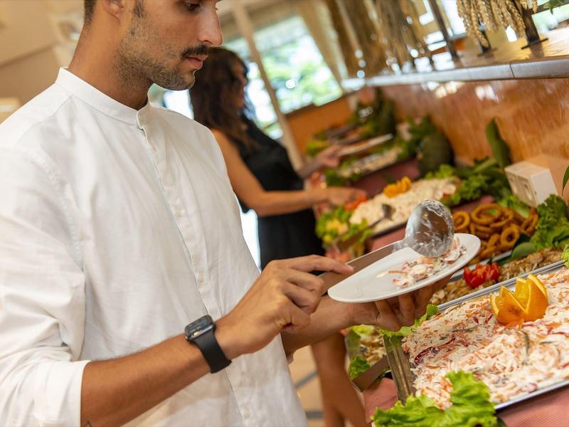 Muž v bílém tričku si bere jídlo z bufetu s různými saláty.