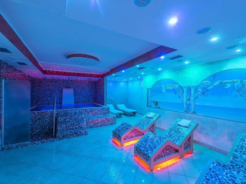 Interiér saunové oblasti s osvětlenými lehátky a dekorativními nástěnnými malbami.