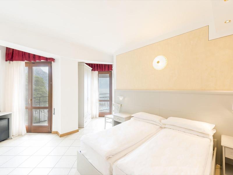 Světý hotelový pokoj se dvěma jednolůžky, psacím stolem a balkonem s červenou záclonou.