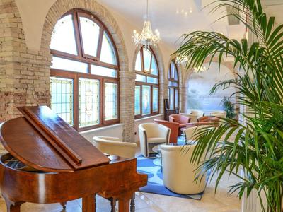 Elegancki salon z fortepianem, wygodnymi fotelami i dużymi łukowymi oknami.