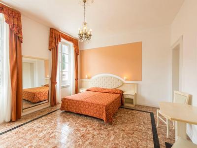 Jasny pokój hotelowy z łóżkiem podwójnym, pomarańczowymi zasłonami i kafelkową podłogą.