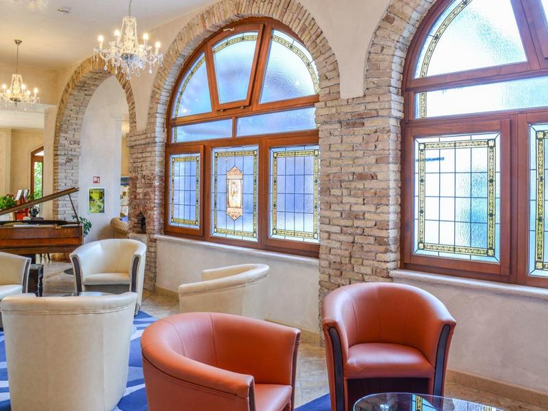 Elegancki salon z skórzanymi fotelami, dużymi łukowatymi oknami i żyrandolami w jasnym otoczeniu.