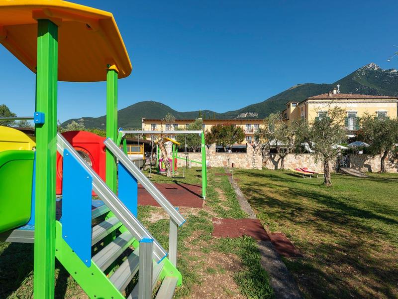 Kolorowy plac zabaw w ogrodzie przed hotelem z górami w tle pod czystym niebem.