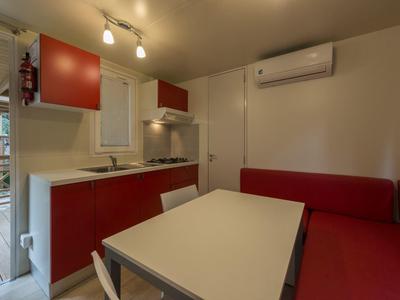 Pequeña cocina con armarios rojos, mesa de comedor y sofá esquinero rojo en habitación moderna.