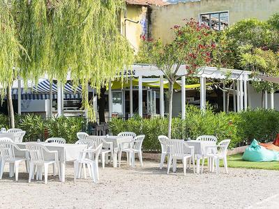 Freiluftrestaurant mit weißen Plastikstühlen und Tischen vor einem Gebäude mit Markisen