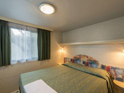 Habitación de hotel pequeña con cama doble, cortina verde y pequeña lámpara de noche.