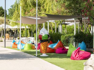 Bunte Sitzsäcke und Sonnenschirme in einem ruhigen Gartenbereich neben einem Gehweg.