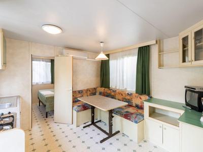 Cocina de hotel luminosa con área de descanso, placa de cocina, cafetera y cortinas verdes.