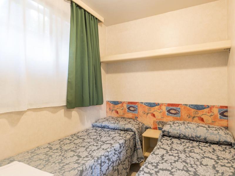 Habitación de hotel pequeña con dos camas individuales, colchas azules estampadas y cortina verde.