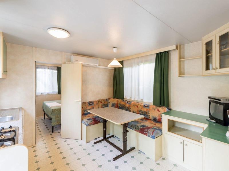 Cocina de hotel luminosa con área de descanso, placa de cocina, cafetera y cortinas verdes.