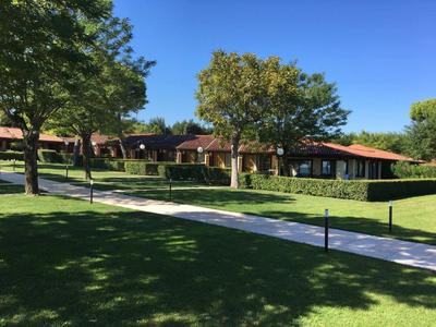 A well-maintained garden with lawn, trees, and a path in front of a single-story building with a red roof.