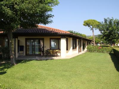 Einfamilienhaus mit rotem Ziegeldach, umgeben von Grünflächen und Bäumen bei klarem Himmel.