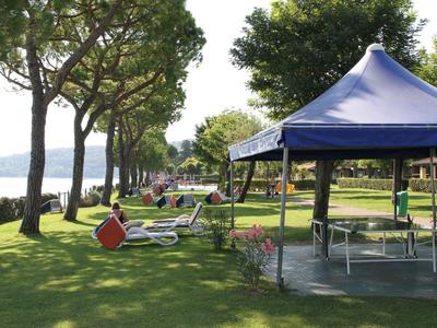 Green lawn with blue sunshades and a view of a lake with trees.