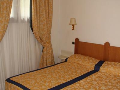 Hotel room with double bed, beige curtains, and a wall lamp.