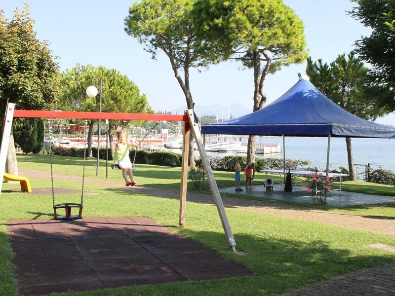 Swing set on grass beside a blue canopy at a hotel with water view.