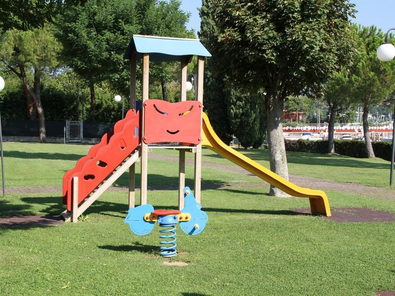 Children's playground with slide, climbing frame, and spring rocker on green grass in a park.