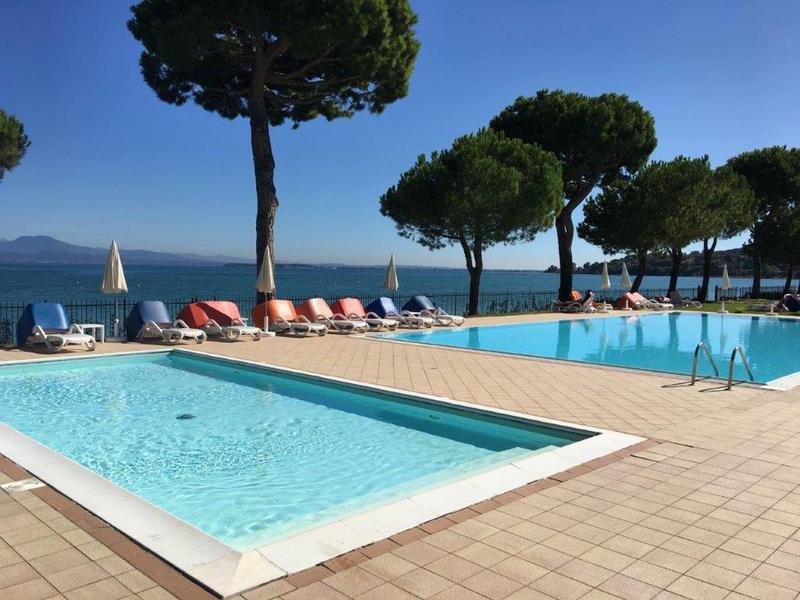 Pool area with lounge chairs and trees by the sea under clear sky