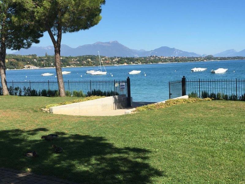Green lawn with trees overlooking a lake with boats under a blue sky.