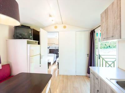 Kleines, helles Wohnmobil mit Küchenzeile, Sitzbereich, Kühlschrank, TV und Zugang zu Schlafzimmer.