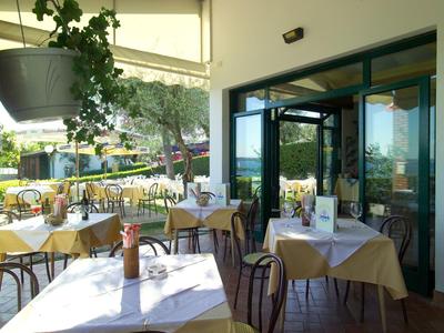 Terrassencafé mit weißen Tischdecken, hängenden Pflanzen und sonnigem Außenbereich.