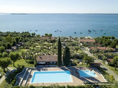Landschaft mit zwei großen Pools, grünem Garten und vielen Booten auf ruhigem blauen See im Hintergrund.