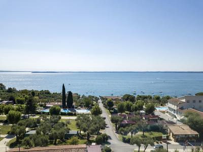 Blick auf ruhigen See mit klar blauem Himmel, Straße und grüner Vegetation im Vordergrund.