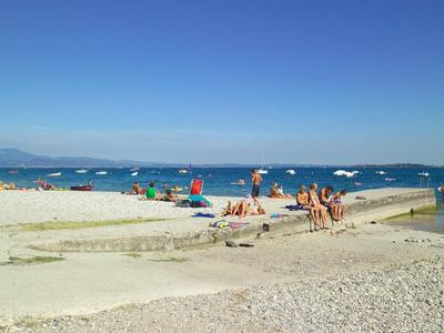 Strand mit Sand, Kies, Menschen, bunten Sonnenschirmen und klarem blauem Himmel.