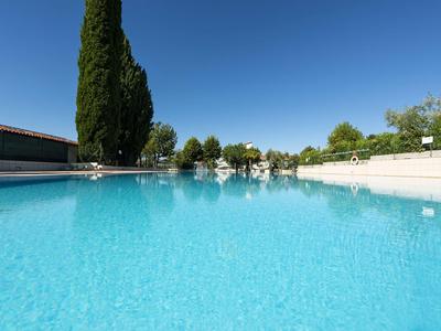 Großer Swimmingpool mit klarem blauem Wasser, umgeben von Bäumen und klarem Himmel.