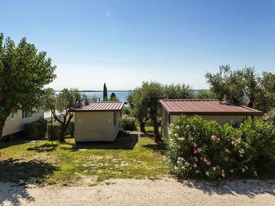 Zwei kleine Holzhäuser mit roten Dächern, umgeben von grünem Gras und Bäumen unter blauem Himmel.
