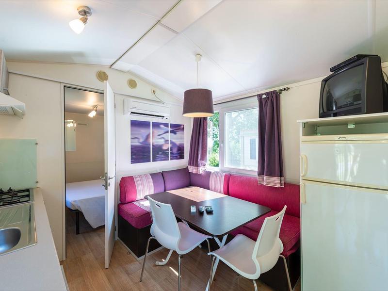 Gemütliche Küchen-Ess-Ecke mit roter Polsterecke, weißen Stühlen, großem Fenster und Küchengeräten.