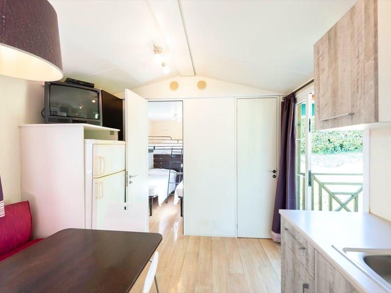 Kleines, helles Wohnmobil mit Küchenzeile, Sitzbereich, Kühlschrank, TV und Zugang zu Schlafzimmer.