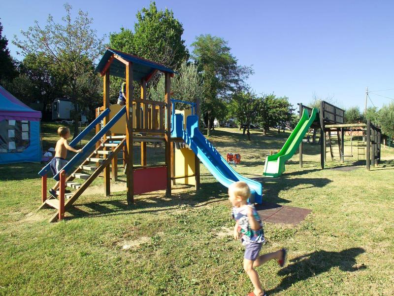 Kinderspielplatz mit Rutschen, Klettergerüsten und grasbewachsenem Boden bei klarem Himmel.