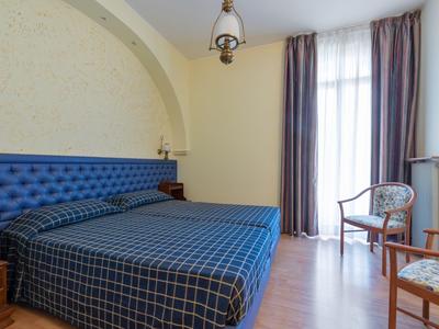 Camera da letto con letto matrimoniale, testiera imbottita blu, finestra con tende e sedia di legno.