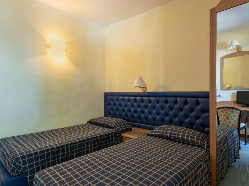 Camera d'hotel con due letti singoli, testiera imbottita e specchio a parete.