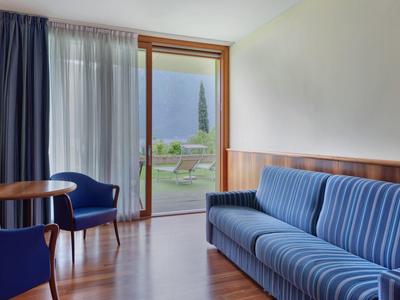 Helles Wohnzimmer mit blau gestreiftem Sofa, zwei blauen Sesseln, Holzwand und Glasfenster mit Blick.