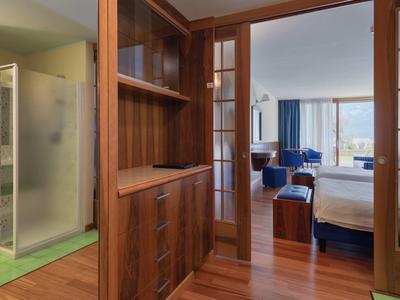 Innenraum mit Holzschrank, Glastür, Schlafzimmer mit Bett, Sessel und blauem Teppich.