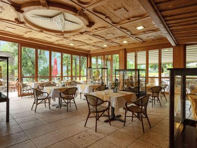 Helles Restaurant mit Holzmöbeln, großen Fenstern und gedeckten Tischen in warmen Farbtönen.