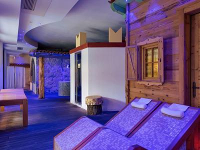 Innenraum mit blauer Beleuchtung, Holzwänden, zwei Liegestühlen und Bänken in entspannter Atmosphäre.
