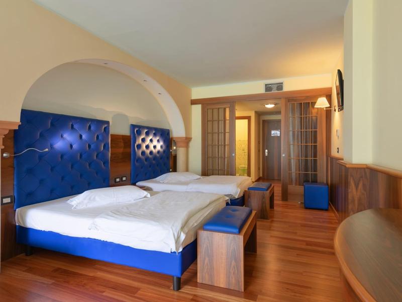 Hotelzimmer mit zwei blauen Betten, Holzboden und warmen Holzdetails, modernes Design.