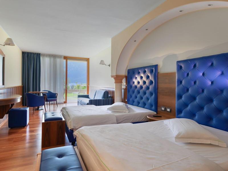 Hotelzimmer mit zwei Einzelbetten, blauen gepolsterten Kopfenden und großem Fenster mit Blick.