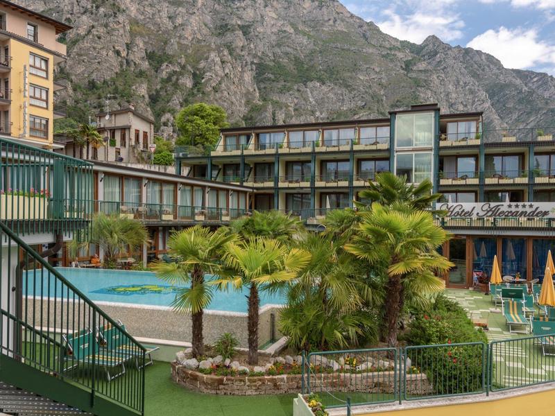 Hotel mit Pool und Palmen vor felsigem Berg unter blauem Himmel mit Wolken.