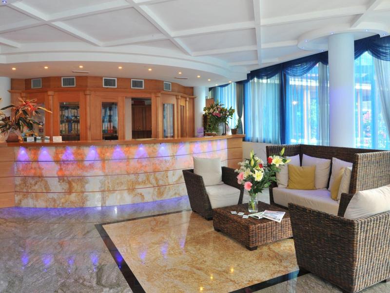 Moderner Hotel-Empfang mit hellbraunem Tresen, Ledersesseln und blauen Vorhängen.