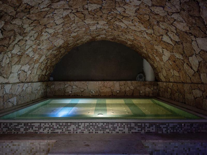 Ein rechteckiger, beleuchteter Pool in einer gewölbten Steinstruktur mit kalksteinfarbenen Wänden.