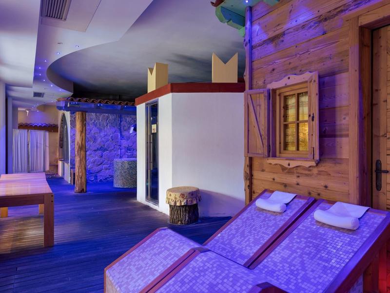 Innenraum mit blauer Beleuchtung, Holzwänden, zwei Liegestühlen und Bänken in entspannter Atmosphäre.