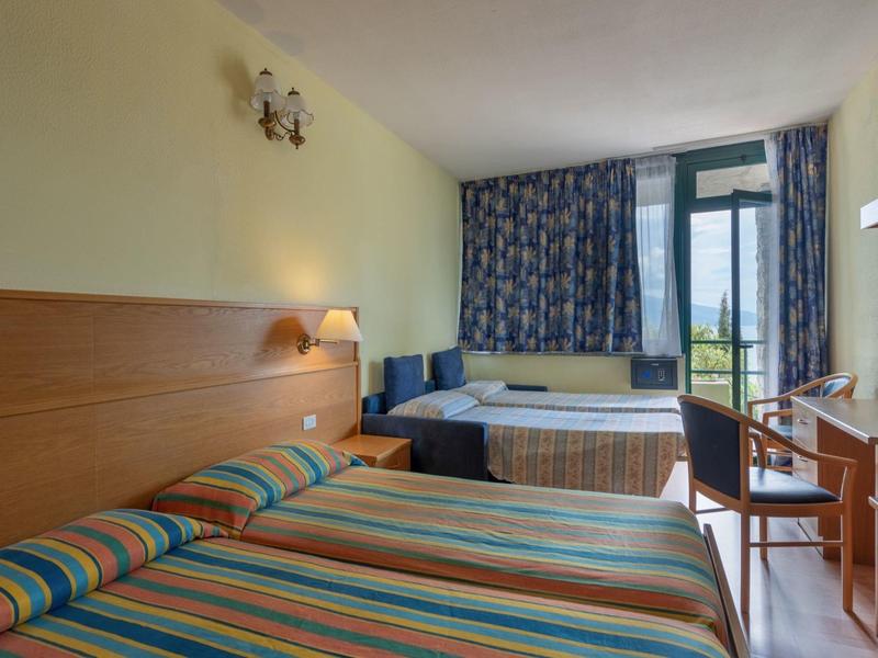 Pokój hotelowy z dwoma łóżkami pojedynczymi, biurkiem i balkonem z widokiem na zielony krajobraz.