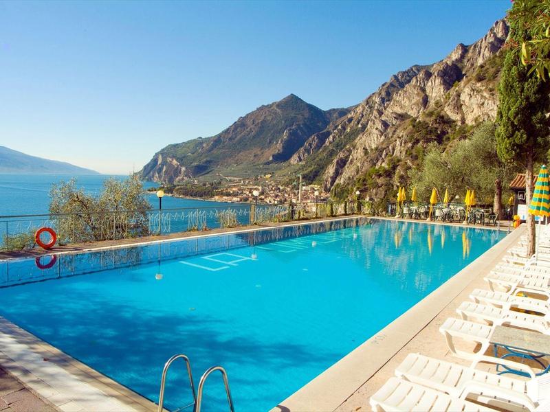 Duży basen z leżakami i górami w tle w słoneczny dzień.