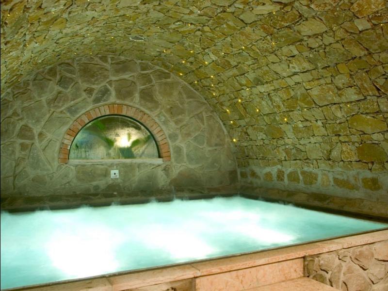 Oświetlone jacuzzi wewnątrz pomieszczenia z kamiennymi sklepieniami i schodami.