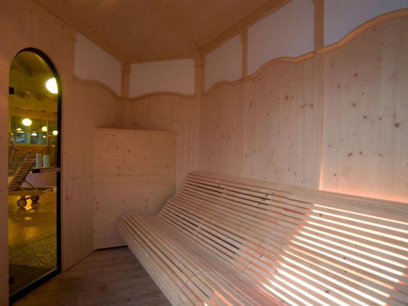 Wnętrze jasnej sauny z drewnianą ławką i światłem wpadającym przez okna.