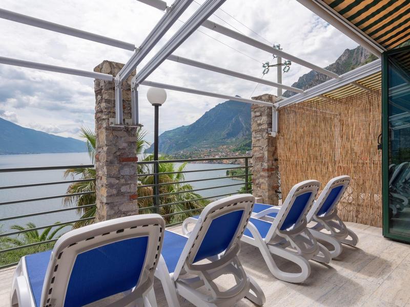 Cztery niebieskie leżaki na balkonie z widokiem na jezioro i góry pod szklanym dachem.